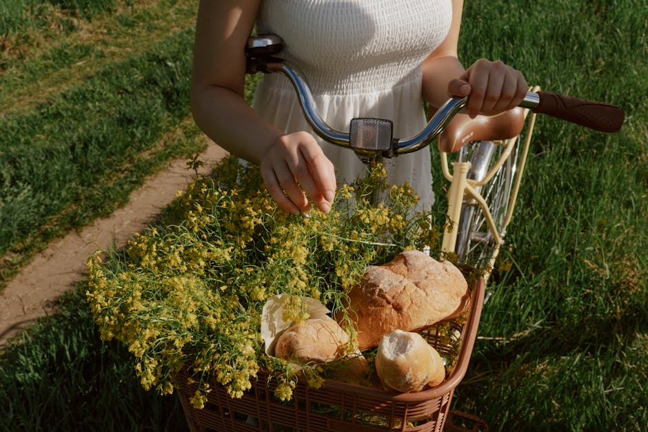 A woman in a white dress with a bicycle basket filled with flowers and bread outdoors. Slow Living