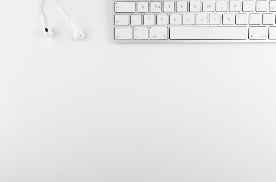 Top view of a white minimalist desk featuring a keyboard and earphones, ideal for technology themes. Digital Minimalism