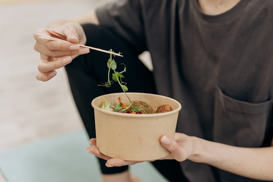 A woman holding a paper bowl filled with a healthy vegetarian meal in an indoor setting, promoting wellness.